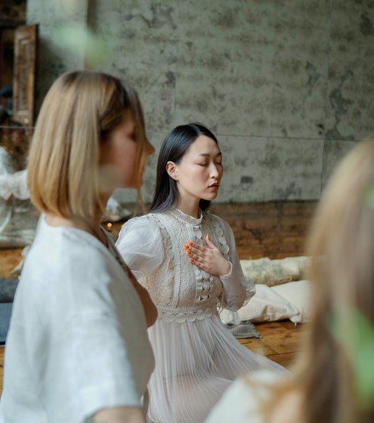 Woman meditating with left hand on her heart, dressed in white