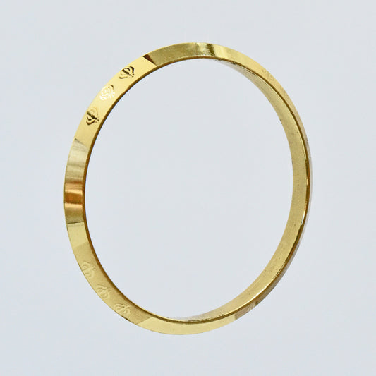 Gold coloured alloy kara with engraved text on a light gray background