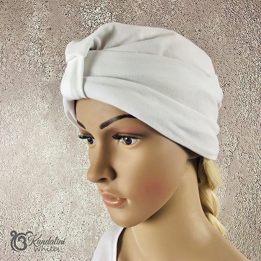 White turban worn by a mannequin head against a textured beige background