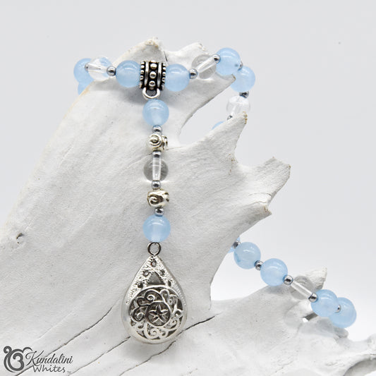 Blue beads and silver teardrop charm on a white shell background