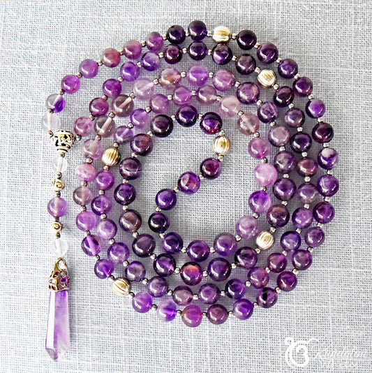 Purple beaded mala with silver accents on a textured gray background