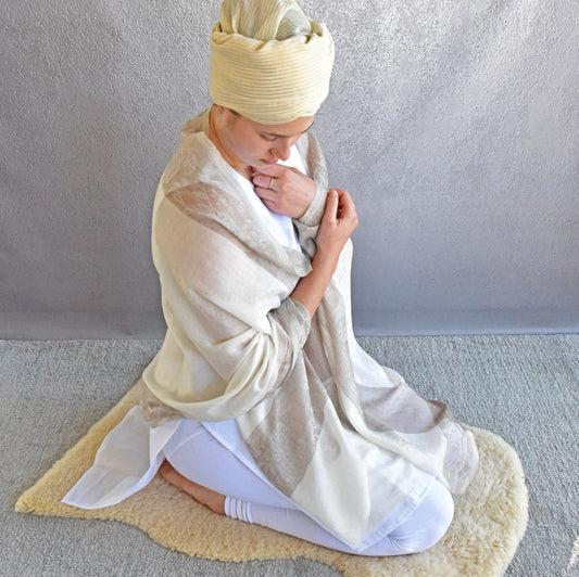 Person wrapped in a white scarf with a yellow headscarf, sitting on a light gray rug.