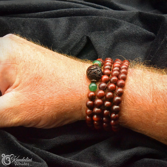 Close-up of a wrist wearing a wooden beaded bracelet with green accents on a black fabric background.