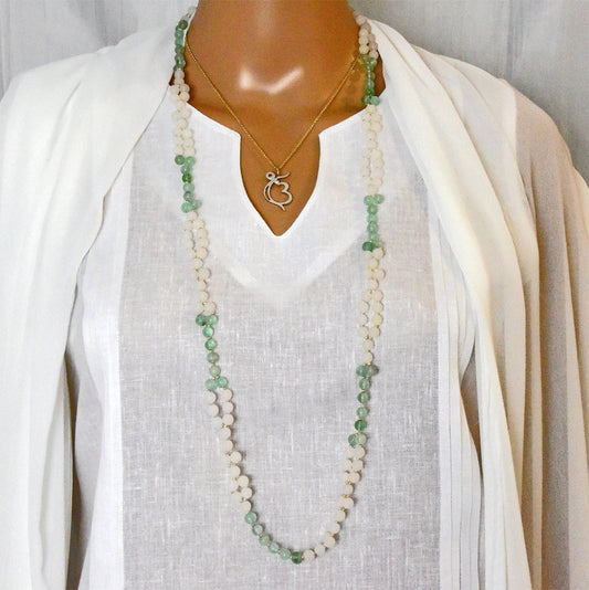 Long beaded necklace with a heart pendant on a mannequin wearing a white top and cardigan.