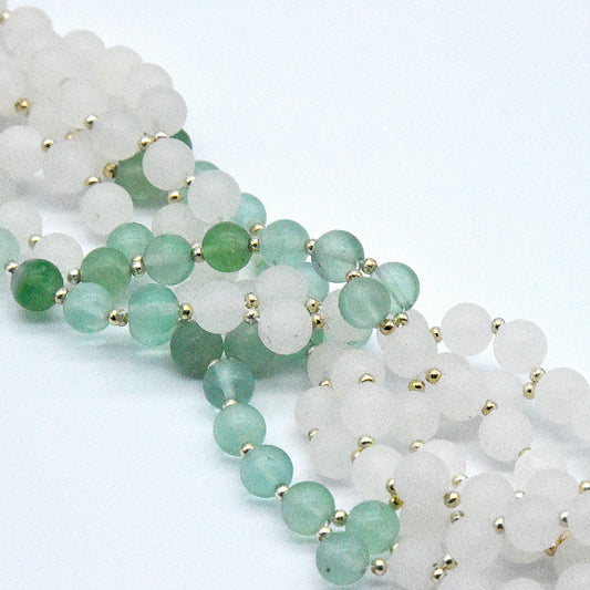 Two strands of green and white beaded jewelry with gold accents on a light gray background.