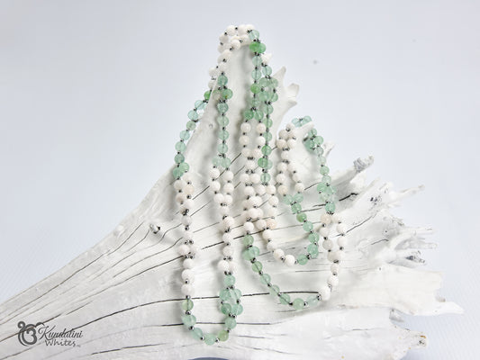 Fluorite and white agate Tantric Mala draped over a white driftwood branch against a light gray background.