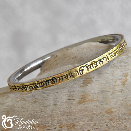 Steel and brass bracelet with engraved text on a wooden surface, featuring the brand 'Kundalini Whites'.