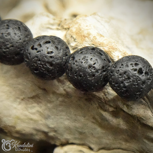 Close-up of a bracelet with black volcanic beads on a textured stone surface, featuring the brand 'Kundalini'.