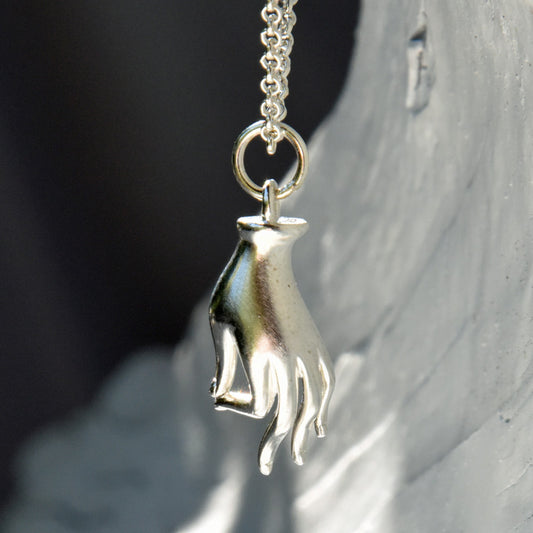 Silver hand-shaped pendant on a chain against a neutral background