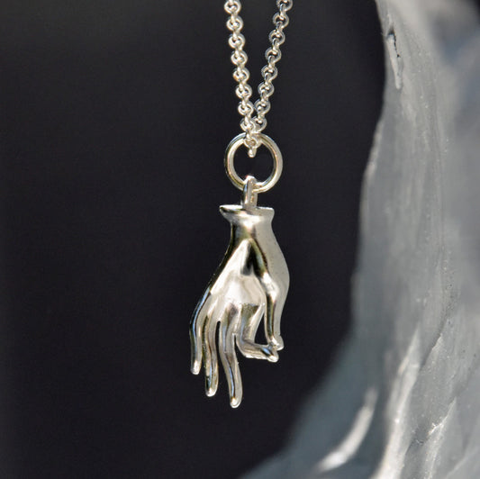 Silver hand-shaped pendant on a chain against a dark background
