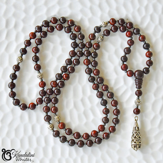 Wooden beaded mala with a silver tassel on a textured white background
