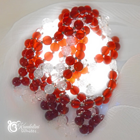 Necklace with red and clear beads on a white fabric, brand 'Kundalini Whites' visible.