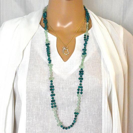 Mannequin wearing a long green beaded necklace with a white top and cardigan.