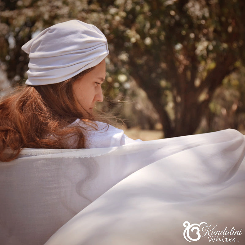 Woman wearing a white headscarf and holding a white cloth outdoors with trees in the background