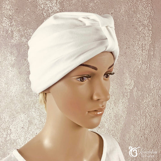 Mannequin head wearing a white towel turban against a textured beige background