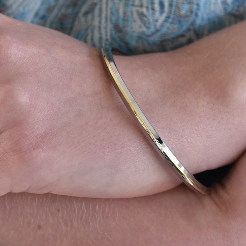 Steel and brass kara bracelet on a wrist with a blue patterned fabric background