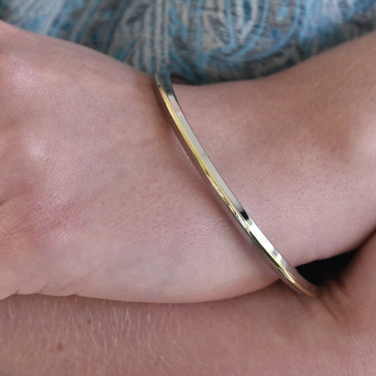 Steel and brass kara bracelet on a wrist with a blue patterned fabric background