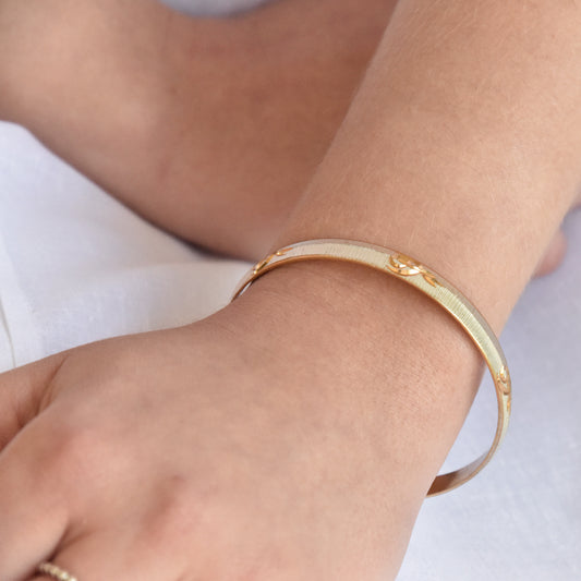 Gold and silver coloured alloy bracelet on a wrist with a blurred background