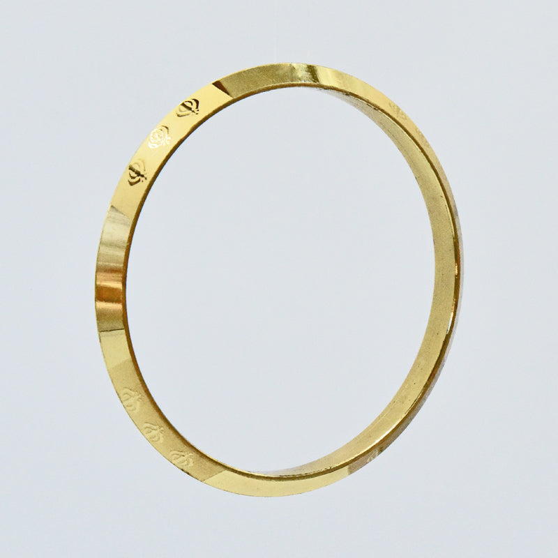 Gold coloured alloy kara with engraved text on a light gray background
