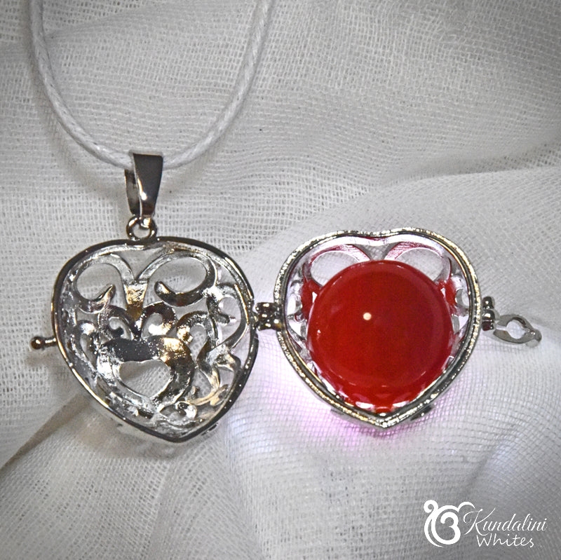 Heart-shaped silver pendant with a red stone on a white fabric background