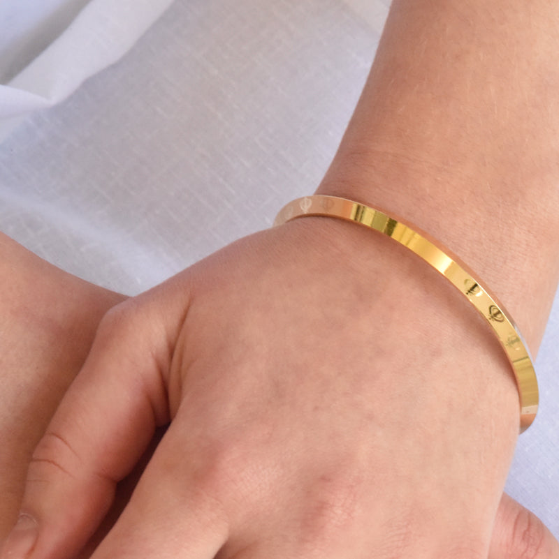 Gold coloured alloy bracelet on a wrist with a white background