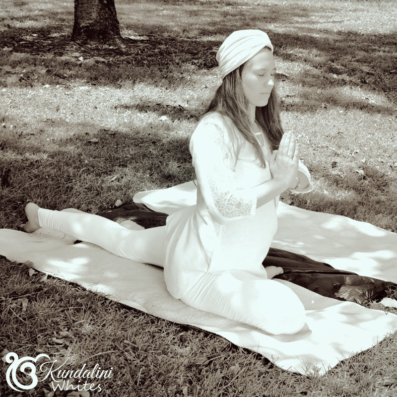 Person in white outfit sitting on a blanket outdoors with 'Kundalini Whites' branding.