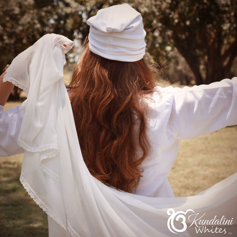 Person wearing a white outfit with long hair, standing outdoors with trees in the background.