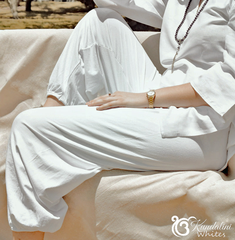 Person wearing a white outfit with a gold watch, sitting on a beige surface.