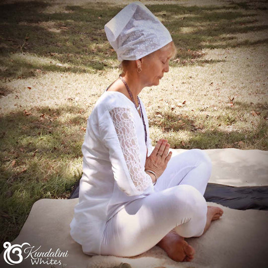 Person in white attire sitting in a meditative pose outdoors.