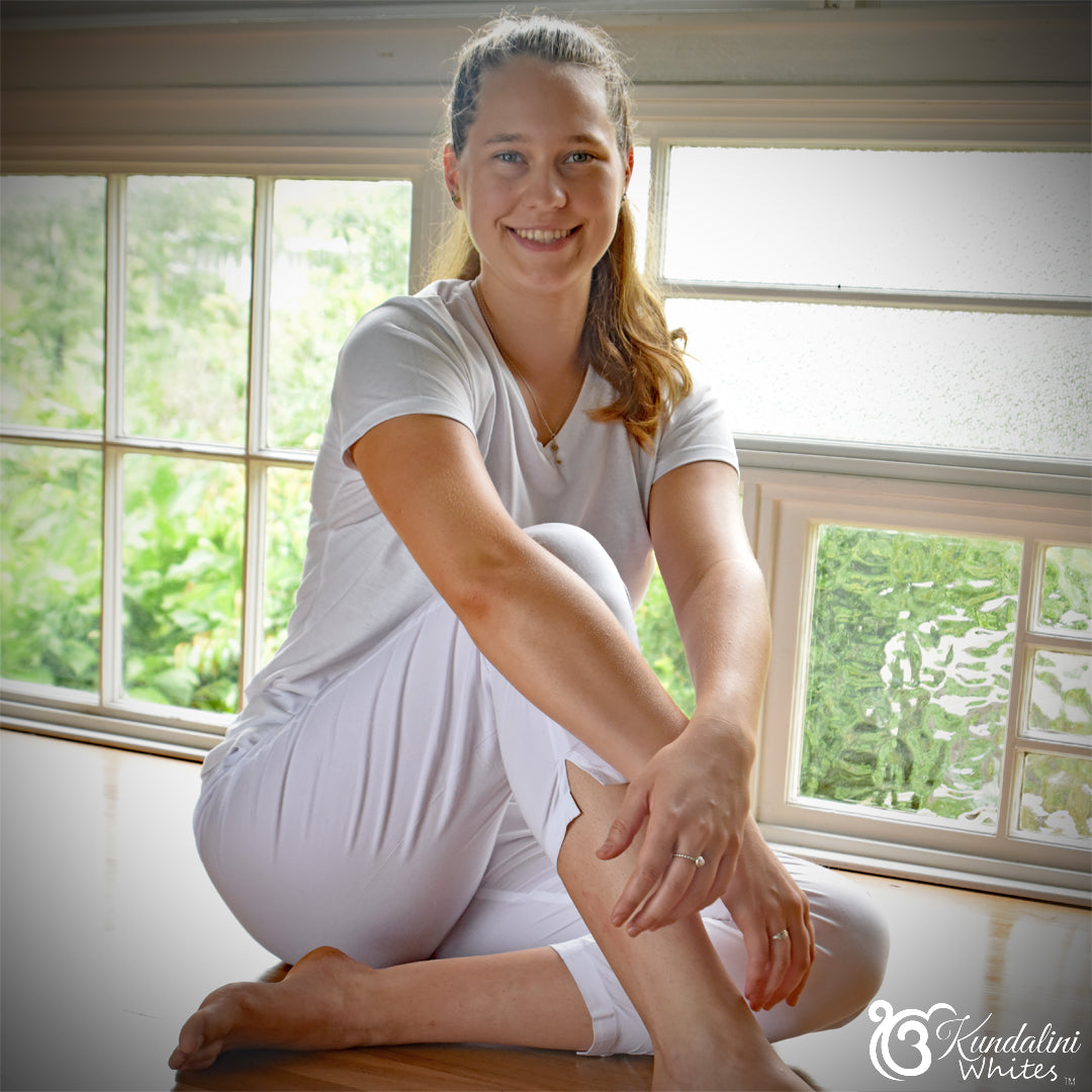 Woman in white outfit sitting on a wooden floor with a window in the background