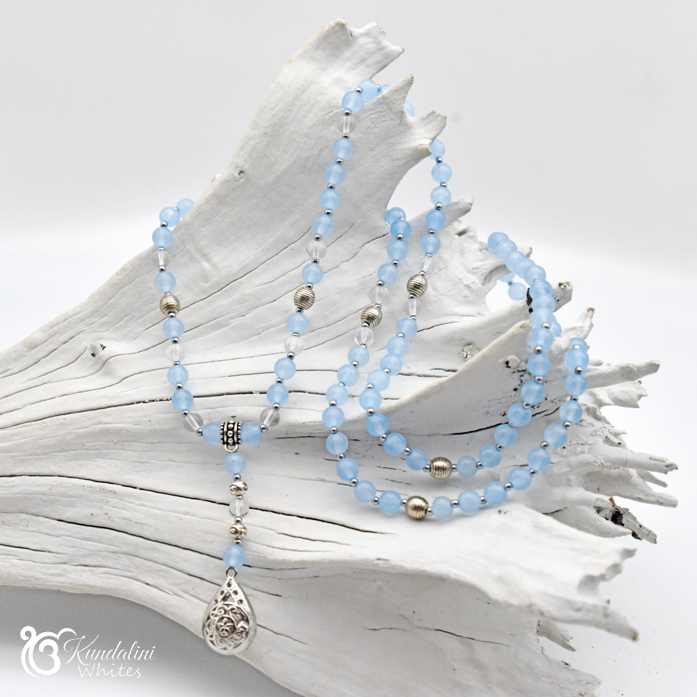 Light blue beaded necklace with silver pendant on a white shell background