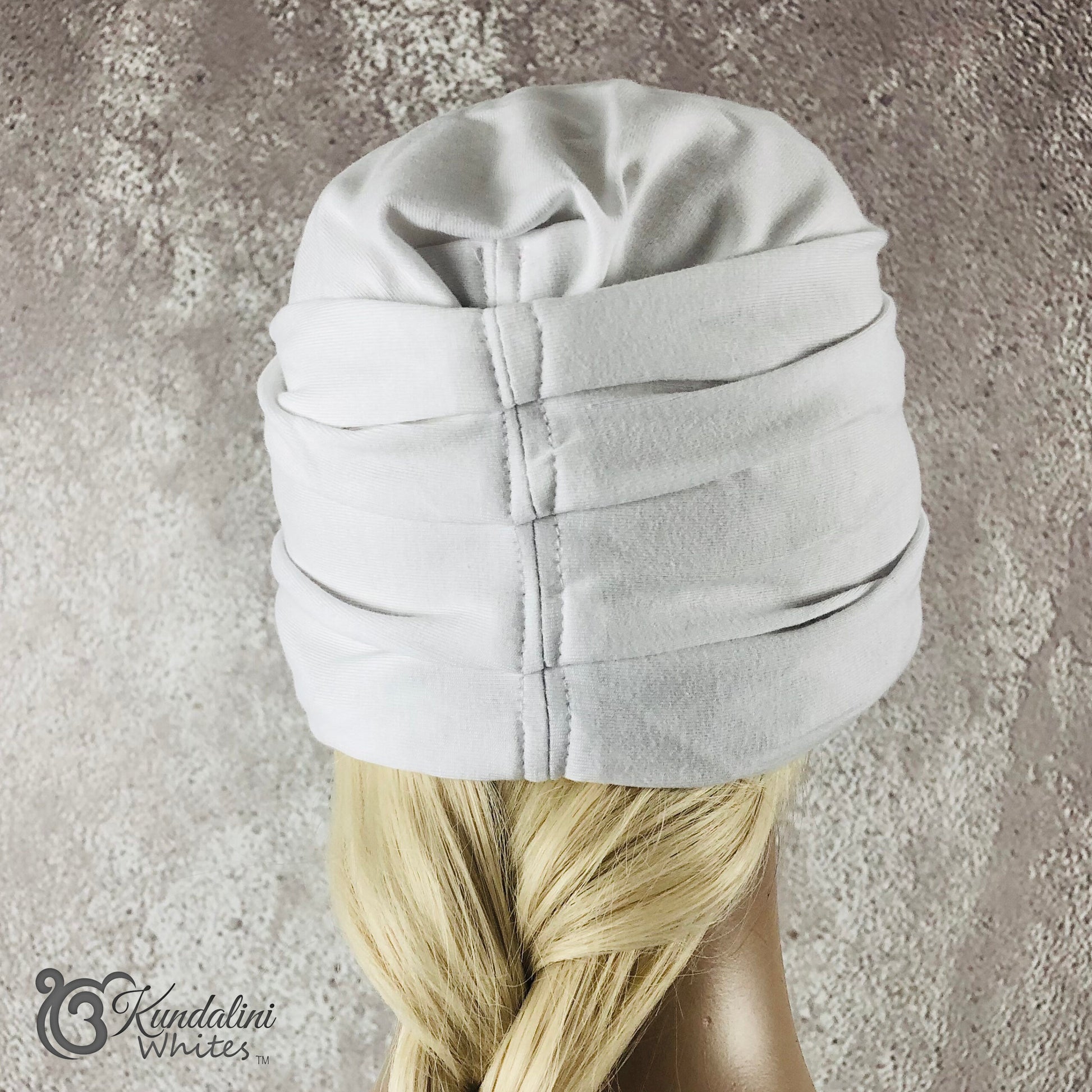White turban on a mannequin head with blonde hair against a textured gray background.