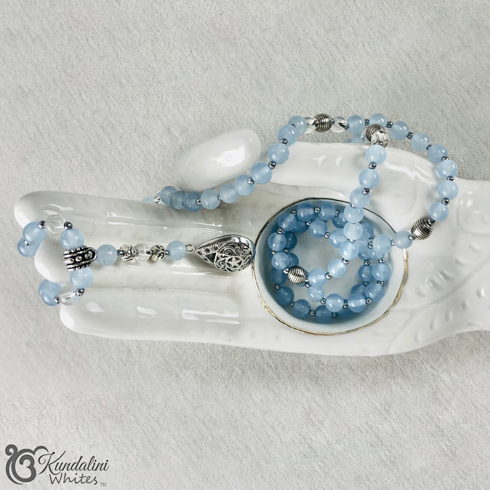 Blue beaded Mala necklace with silver accents on a white dish against a light gray background