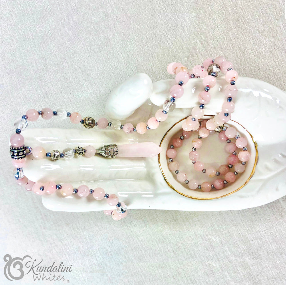 Rose quartz mala necklace on a white dish with 'Kundalini Whites' branding.