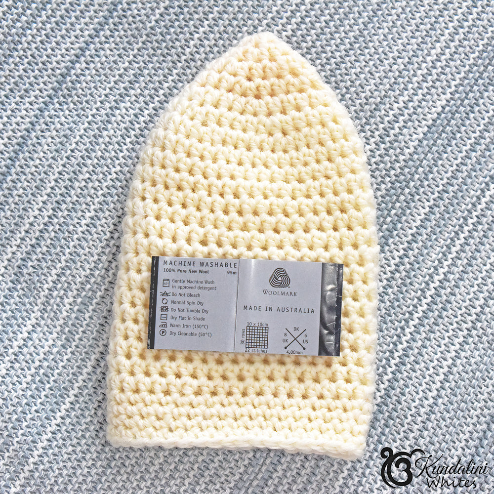 Crocheted offwhite woollen mesh cap with a label on a textured gray background