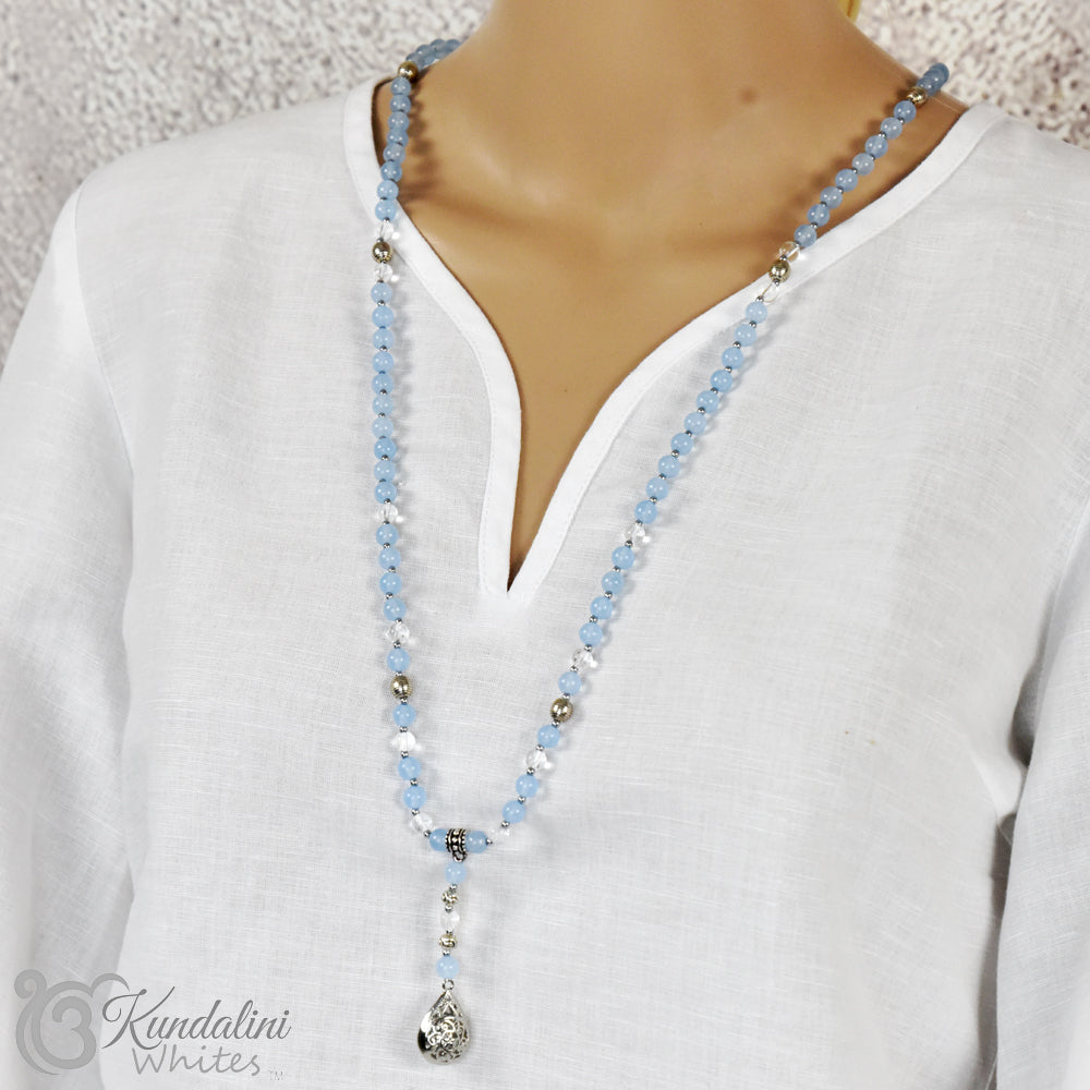 Necklace with blue beads and a teardrop pendant on a white shirt, brand 'Kundalini Whites' visible.