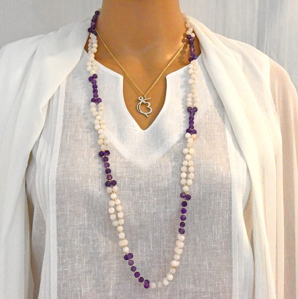 Long beaded necklace with purple and white beads on a mannequin wearing a white top.