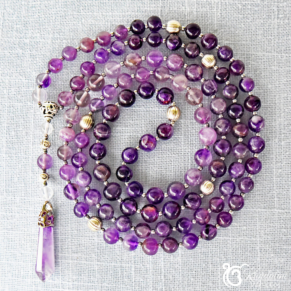 Purple beaded mala with silver accents on a textured gray background