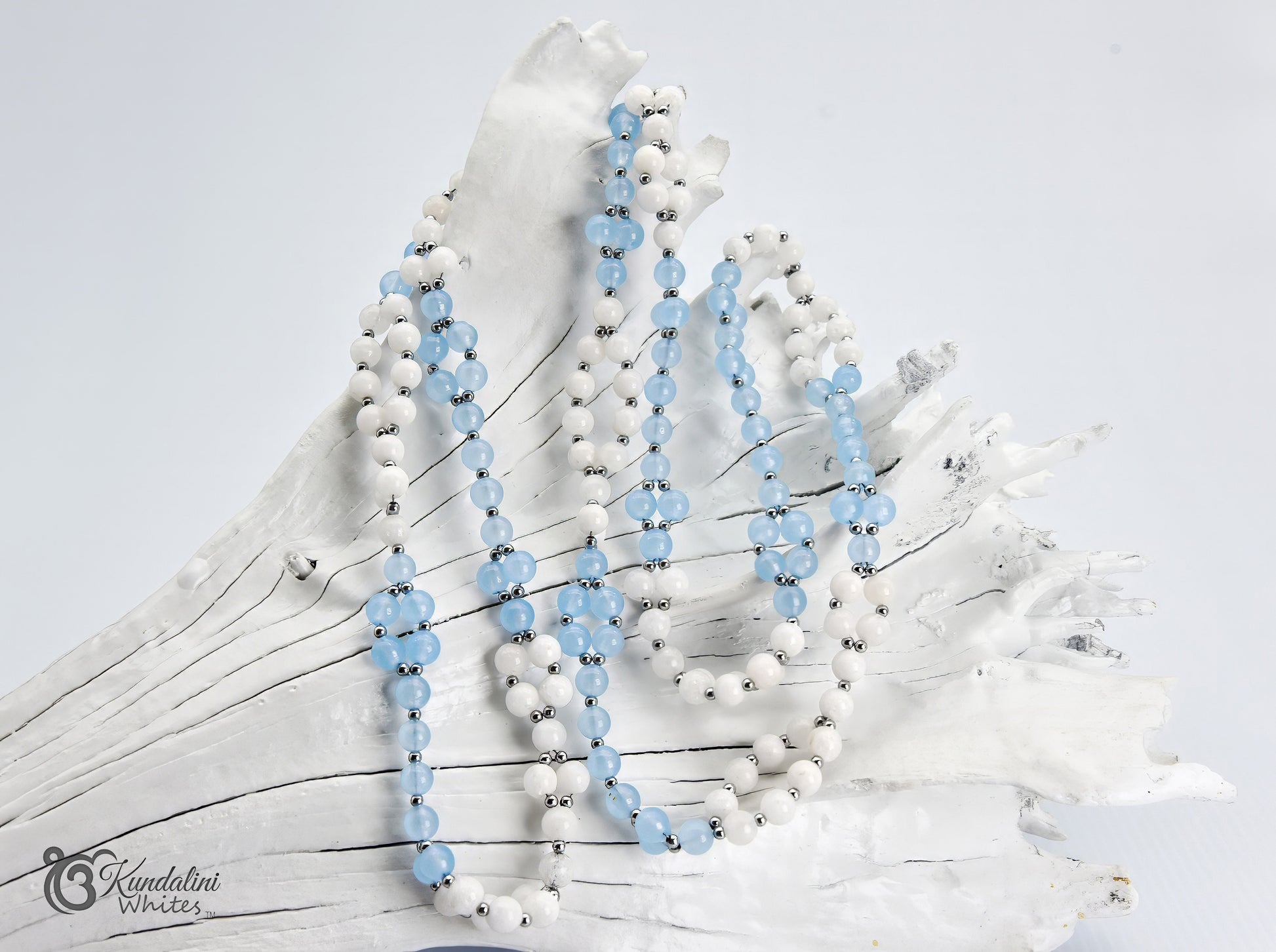 An aquamarine and white agate Tantric Mala, draped over a white decorative driftwood prop on a plain white background. A watermark for 'Kundalini Whites' is visible in the bottom-left corner.