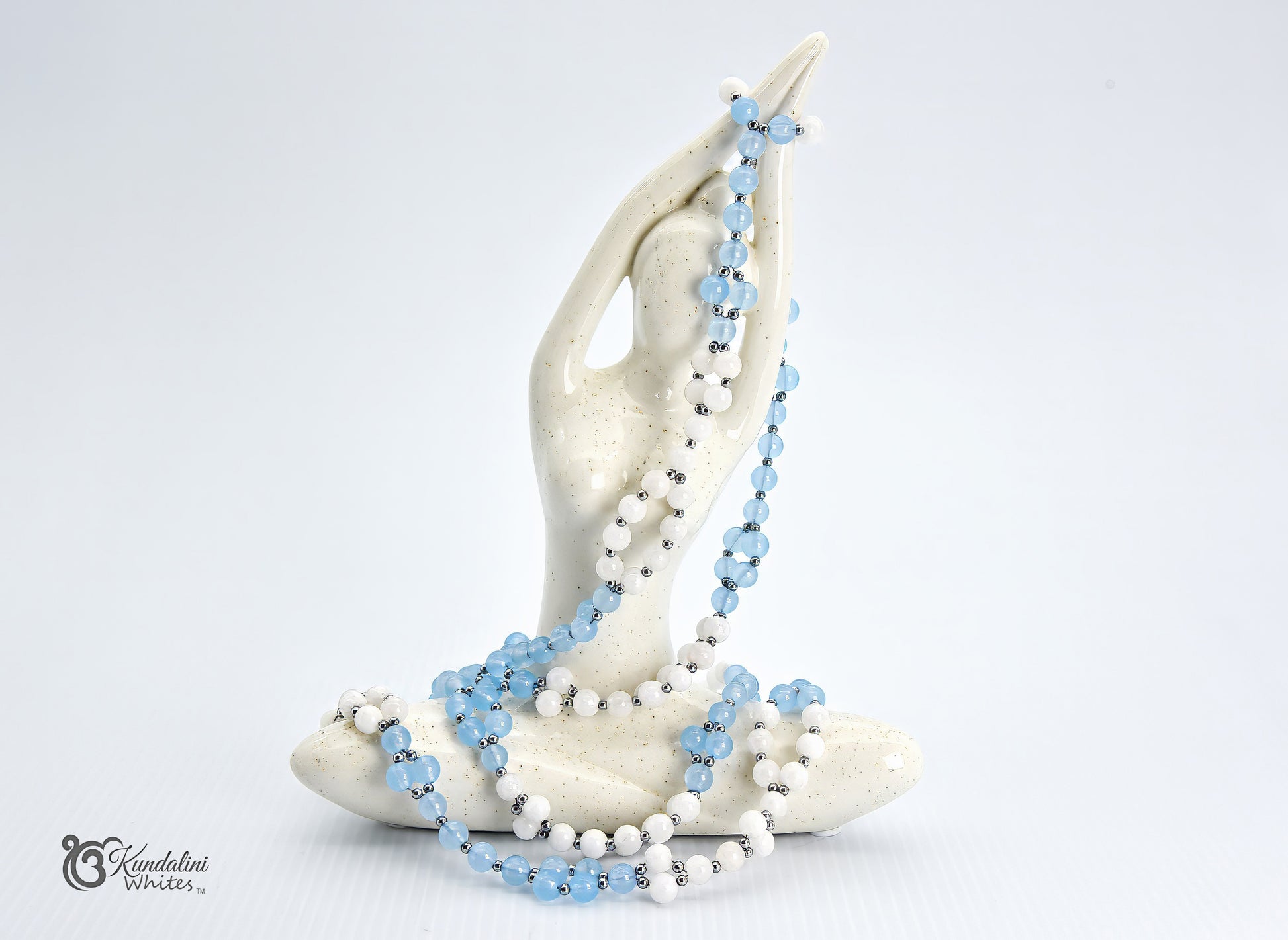 An aquamarine and white agate Tantric Mala draped over a white ceramic hand statue, set against a clean white background.