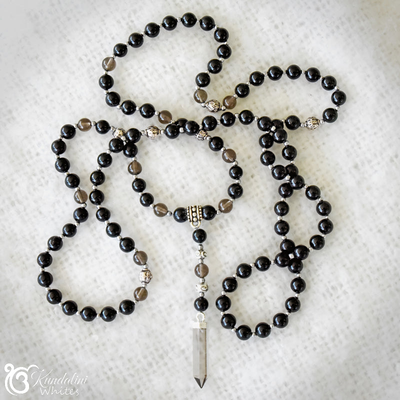 Black beaded Mala necklace with a crystal pendant on a white textured background