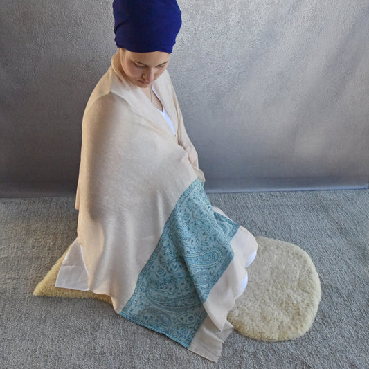 Person wrapped in a white and blue patterned blanket sitting on a gray floor.