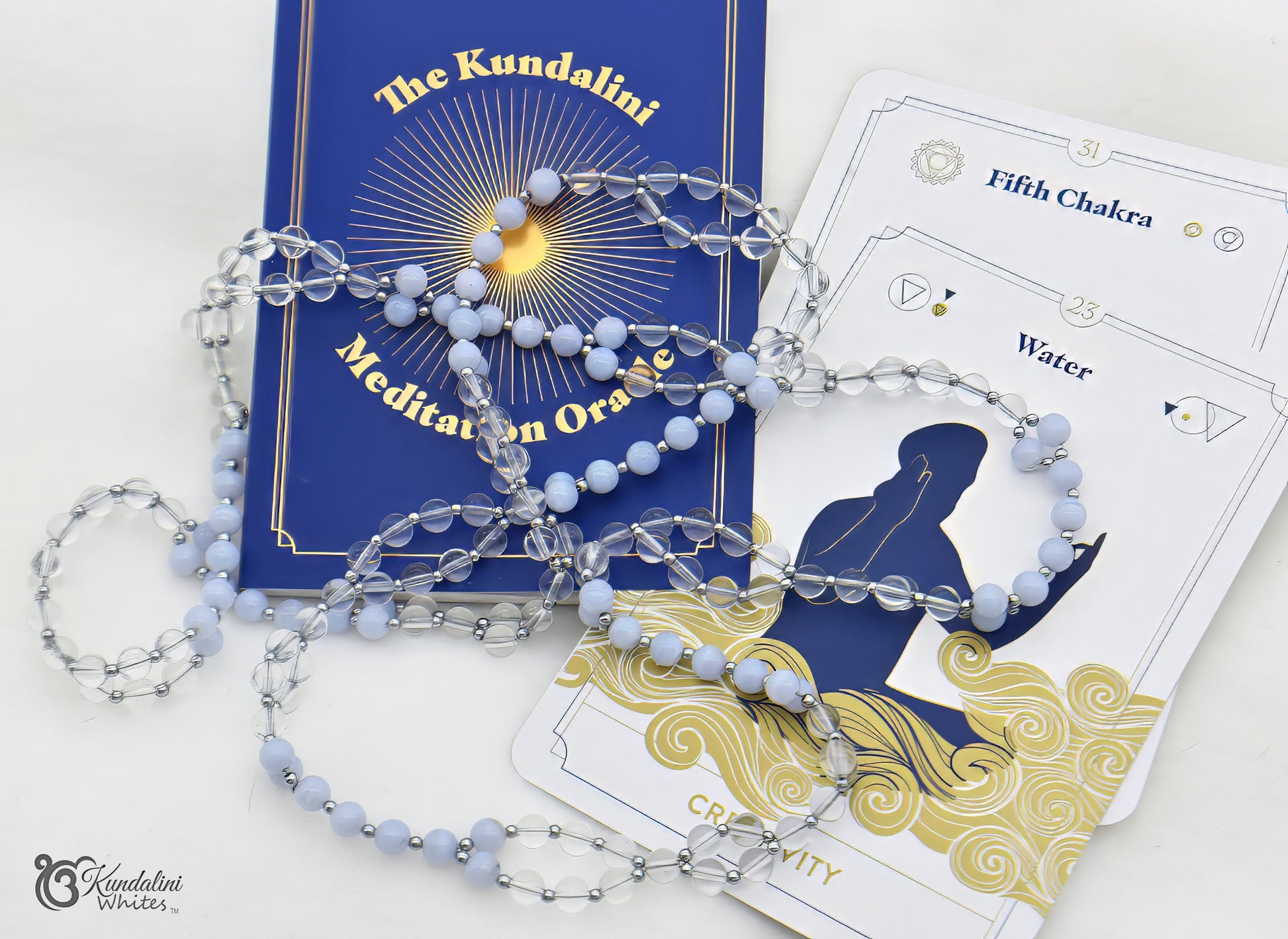 Blue tantric necklace on a white surface with 'The Kundalini' book and cards.