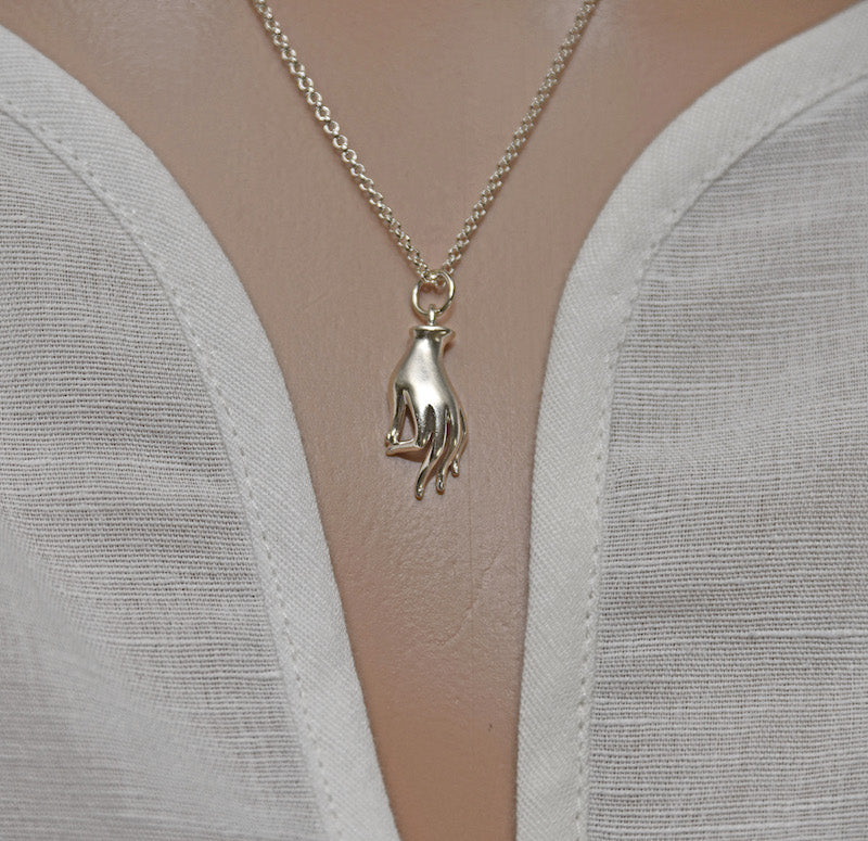 Silver necklace with a hand-shaped pendant on a mannequin wearing a white top.