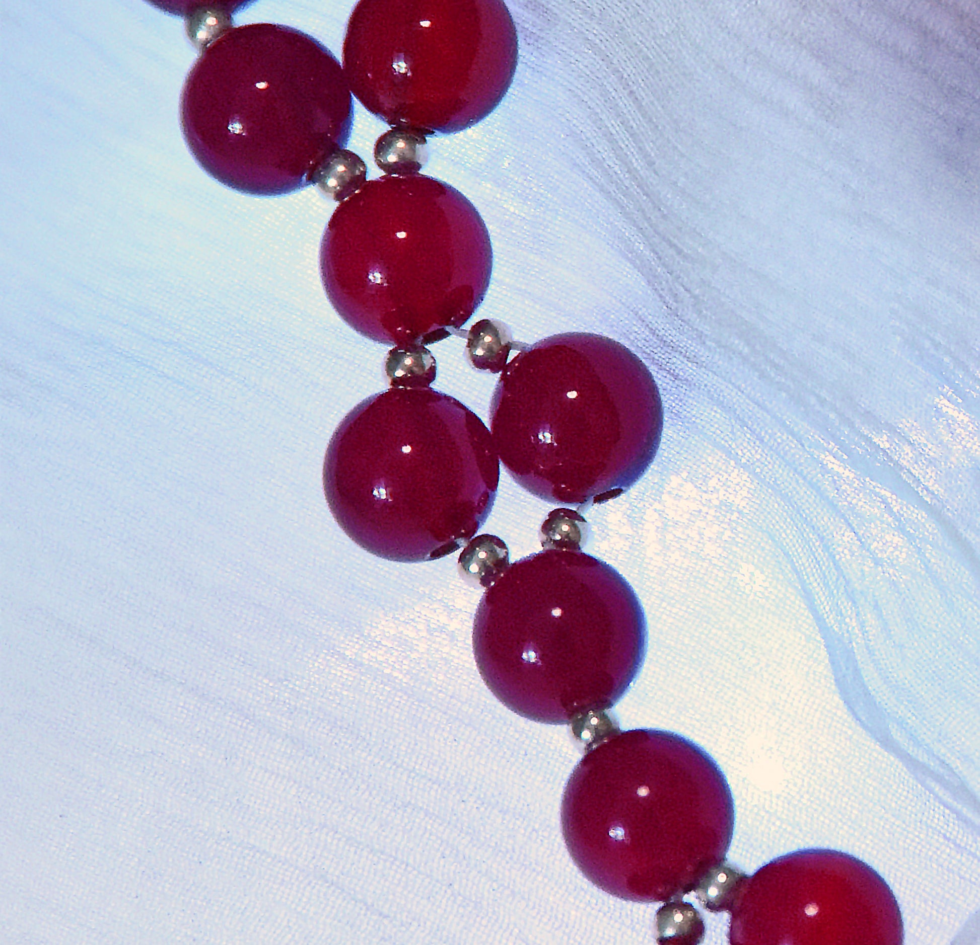 Necklace with red beads and silver accents on a textured white background