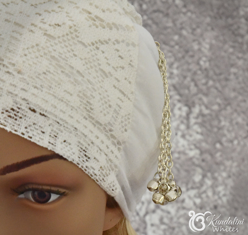Close-up of a silver chain decoration worn by a person with a white turban, with a blurred background.