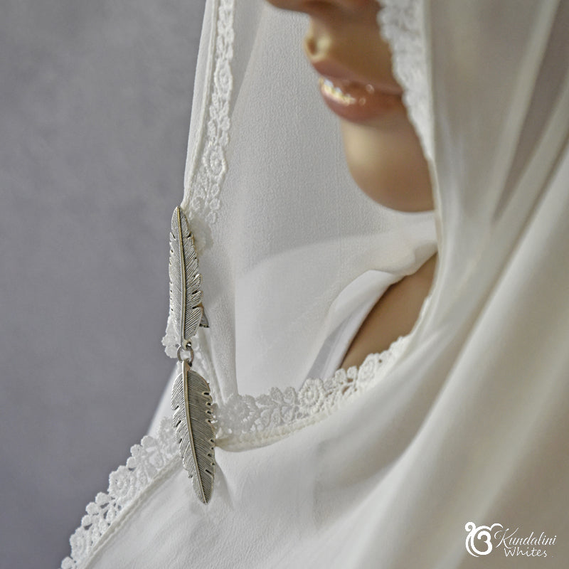 Close-up of a white chunni with lace details and a feather accessory against a gray background.