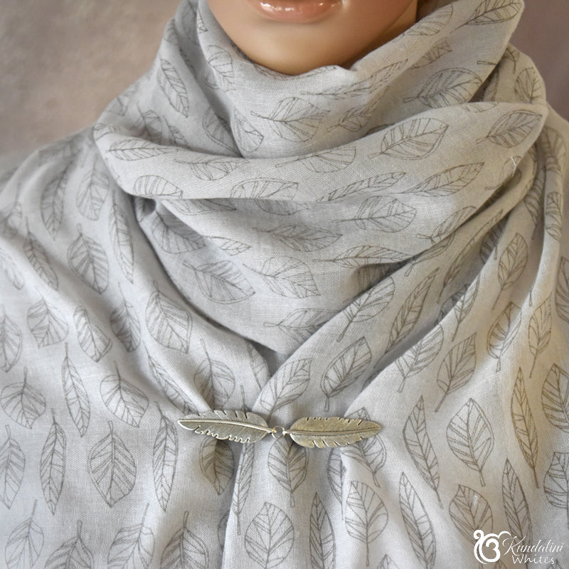 Gray scarf with leaf pattern and feather accessory on a mannequin