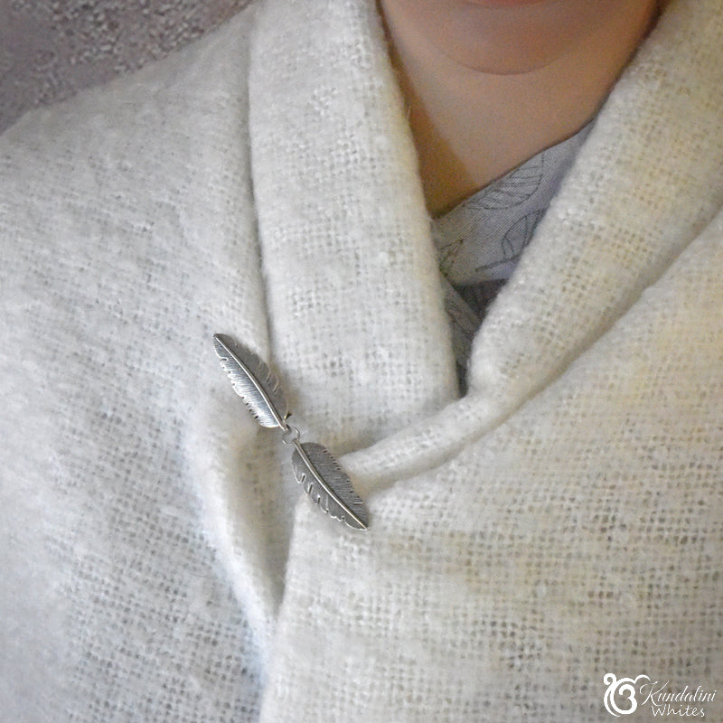 Person wearing a white scarf with a decorative brooch on a neutral background