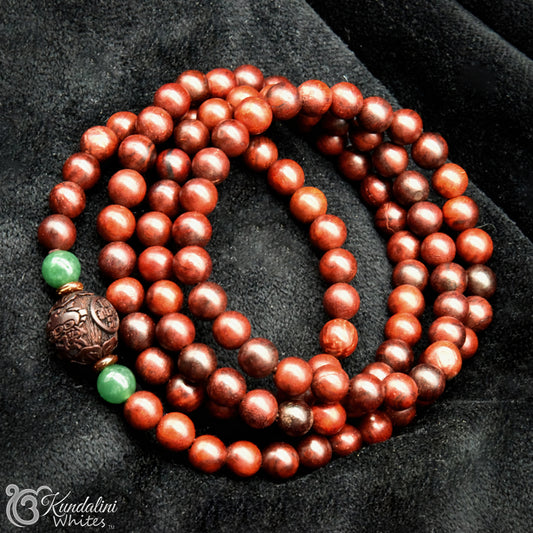 Brown wood beaded necklace with a green gemstone on a dark fabric background